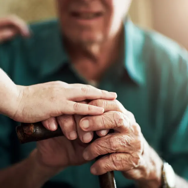 Caregiver gently holding an older man’s hands