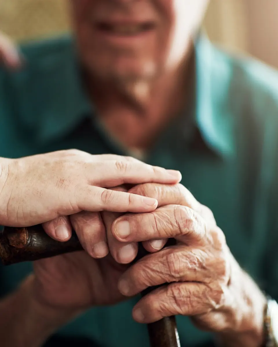 Caregiver’s hand resting gently on an older man’s hands