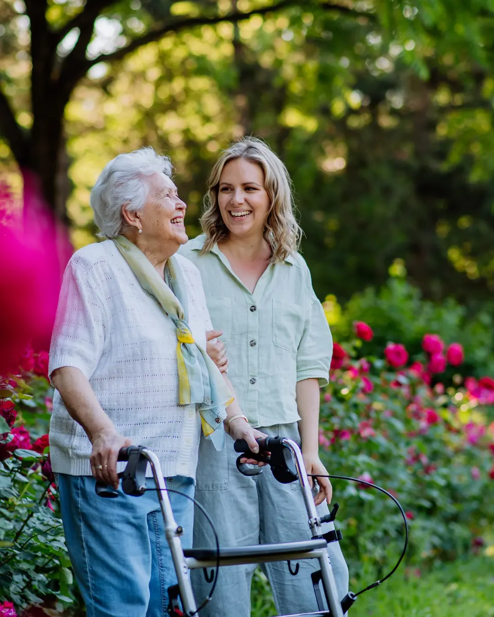 Smiling senior woman with a walker and her caregiver in a garden